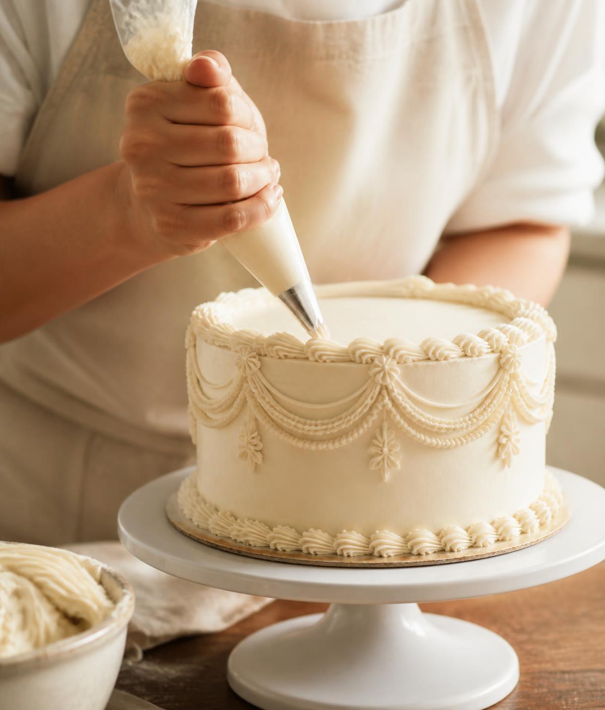 Hands piping fine buttercream detail onto an ivory Grace cake